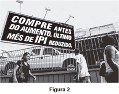 Figura 2: Fotografia de um ambiente urbano, destacando-se um grande outdoor publicitário com a mensagem promocional em letras garrafais: 'COMPRE ANTES DO AUMENTO. ÚLTIMO MÊS DE IPI REDUZIDO.'. Ao fundo e abaixo do outdoor, notam-se carros expostos e pedestres caminhando.
