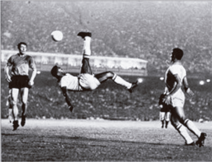 Fotografia em preto e branco de um jogo de futebol no estádio do Maracanã. O jogador Pelé está no ar realizando um movimento clássico de 'bicicleta', chutando a bola que está acima dele. Outros jogadores observam a jogada.