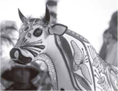 Fotografia em preto e branco focada na cabeça e no pescoço de uma figura representativa do Bumba meu boi. A estrutura é ricamente ornamentada com bordados complexos que incluem formas geométricas, linhas e desenhos que lembram folhas ou flores.