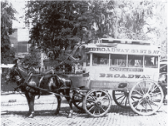 Fotografia em preto e branco mostrando uma carruagem de transporte coletivo puxada por cavalos na rua.