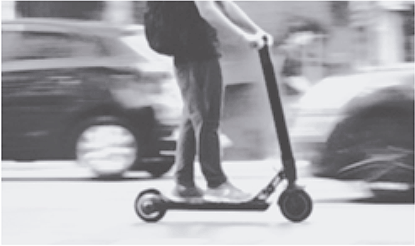 Fotografia em preto e branco de uma pessoa andando em um patinete elétrico na rua, com carros ao fundo.