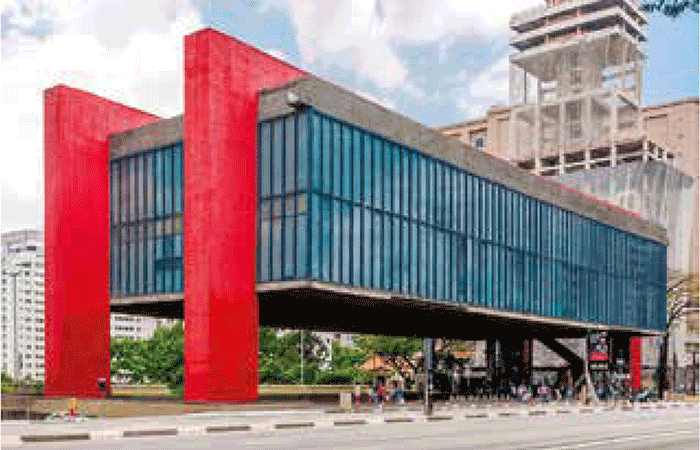 Fotografia do Museu de Arte de São Paulo (MASP), localizado na Avenida Paulista. O edifício moderno apresenta um grande volume retangular de vidro e concreto suspenso por quatro pilares vermelhos, criando um icônico vão livre.